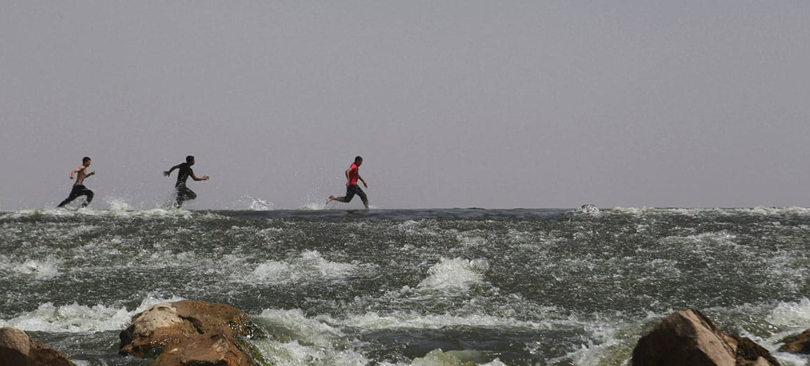 North Africa. Three young men running on a surface of water with rocks.