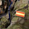 Close-up of two soldiers in camouflage uniforms. One has a Spanish flag patch on their shoulder, and the other has a NATO Latvia patch, representing collaboration within the NATO alliance. Defence